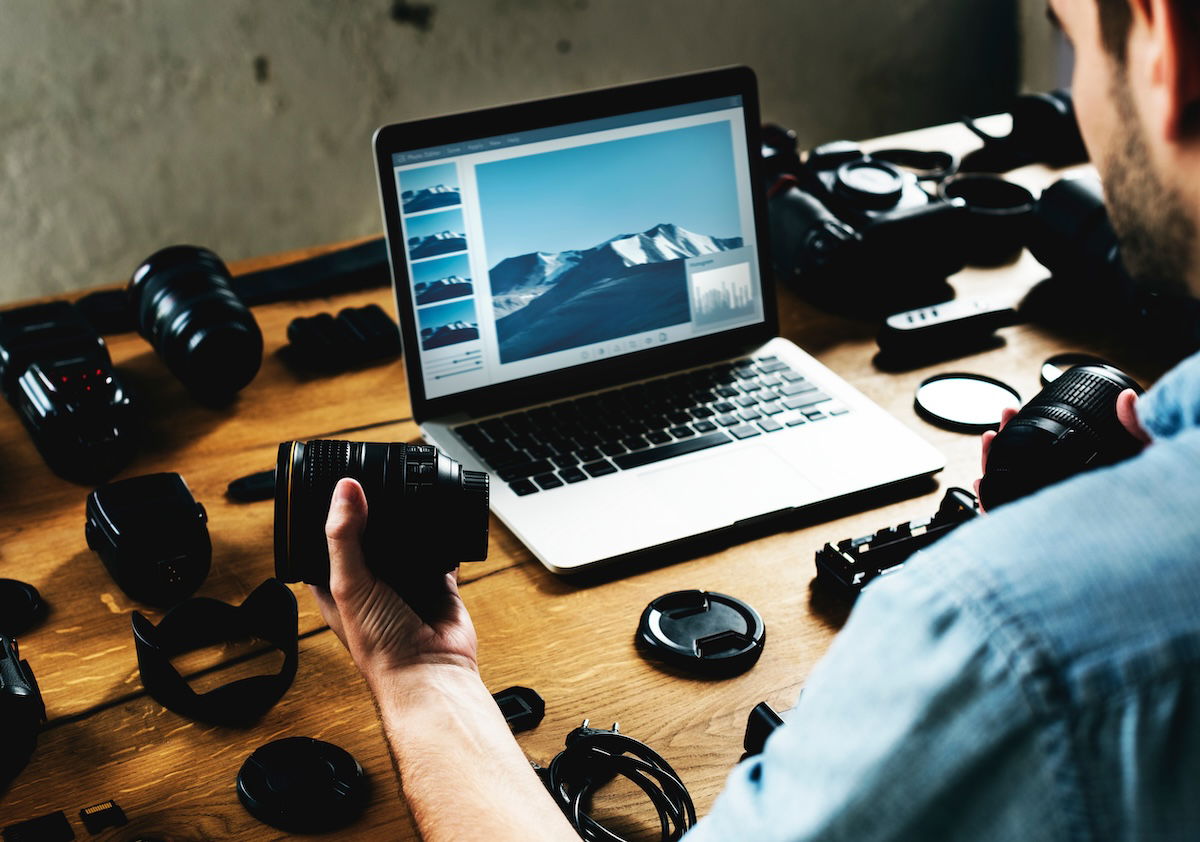 A person editing pictures on a laptop with camera equipment around